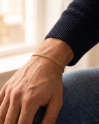 Men's gold Cuban chain bracelet worn on the wrist with a navy knit sweater