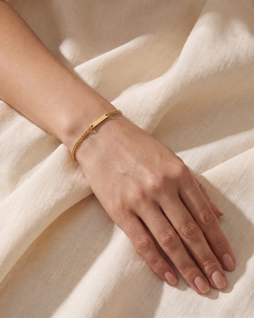 Delicate 18K gold Cuban chain bracelet on a woman's wrist resting on ivory linen