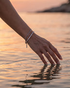 Fine silver Cuban bracelet stacked with a silver tennis bracelet at the sea at sunset