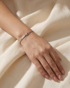 Delicate silver Cuban chain bracelet on a woman's wrist resting on ivory linen
