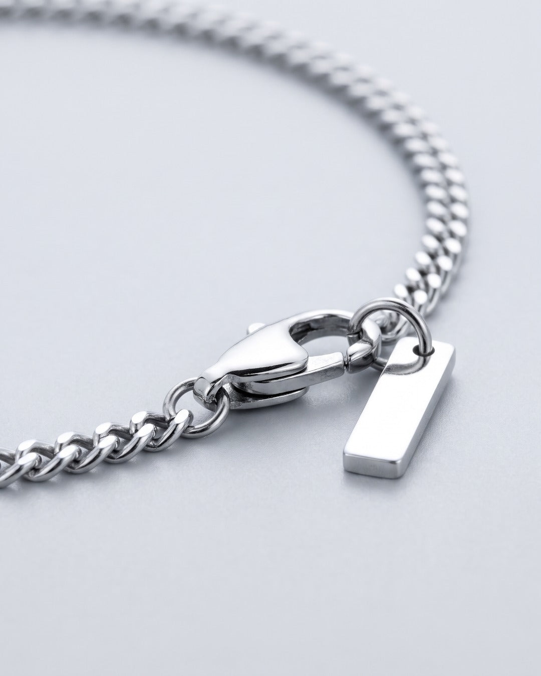 Macro close-up of fine silver Cuban links, lobster clasp and bar tag
