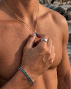 Aquamarine pendant necklace, 1 carat, 18K gold — held between the fingers in beach light