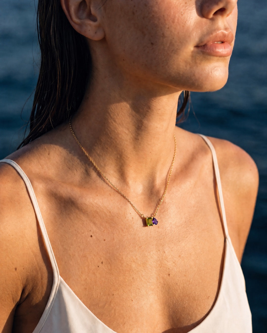 August birthstone necklace in 14K gold, peridot green and violet stones, worn