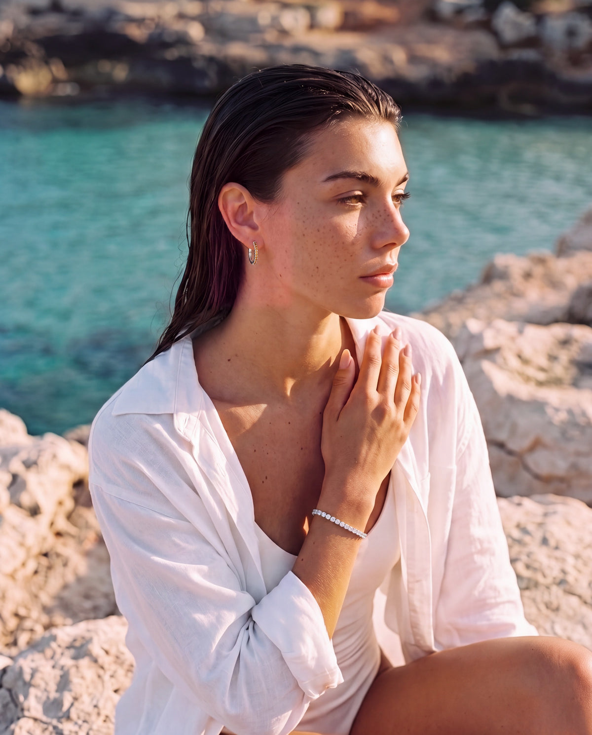 Model wearing the citrine silver Lumière huggies by the sea