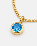 Close-up of the blue topaz bezel pendant on the gold Lumière necklace