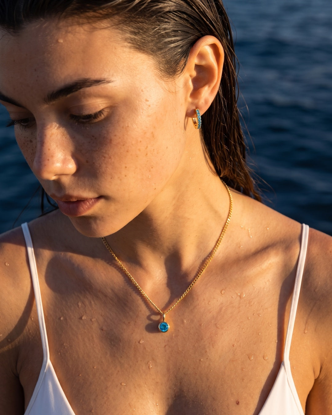 Blue Topaz gold Lumière necklace worn with matching huggie earrings