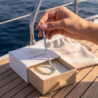 Hand lifting a Pureform gold tennis bracelet from its ivory gift box