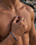 Royal Blue pendant necklace, 2 carat, 18K gold — held between the fingers in beach light