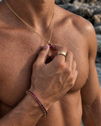 Ruby pendant necklace, 2 carat, 18K gold — held between the fingers in beach light